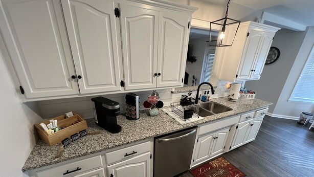 Una cocina con armarios blancos, encimera de granito, cafetera, tostadora y un lavabo.