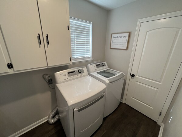 A laundry room with two washing machines, a dryer, and a window with blinds.