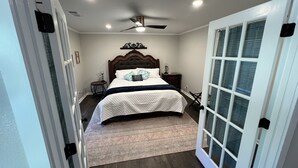 Un dormitorio con cama, ventilador de techo, mesita de noche y ventana con persianas.