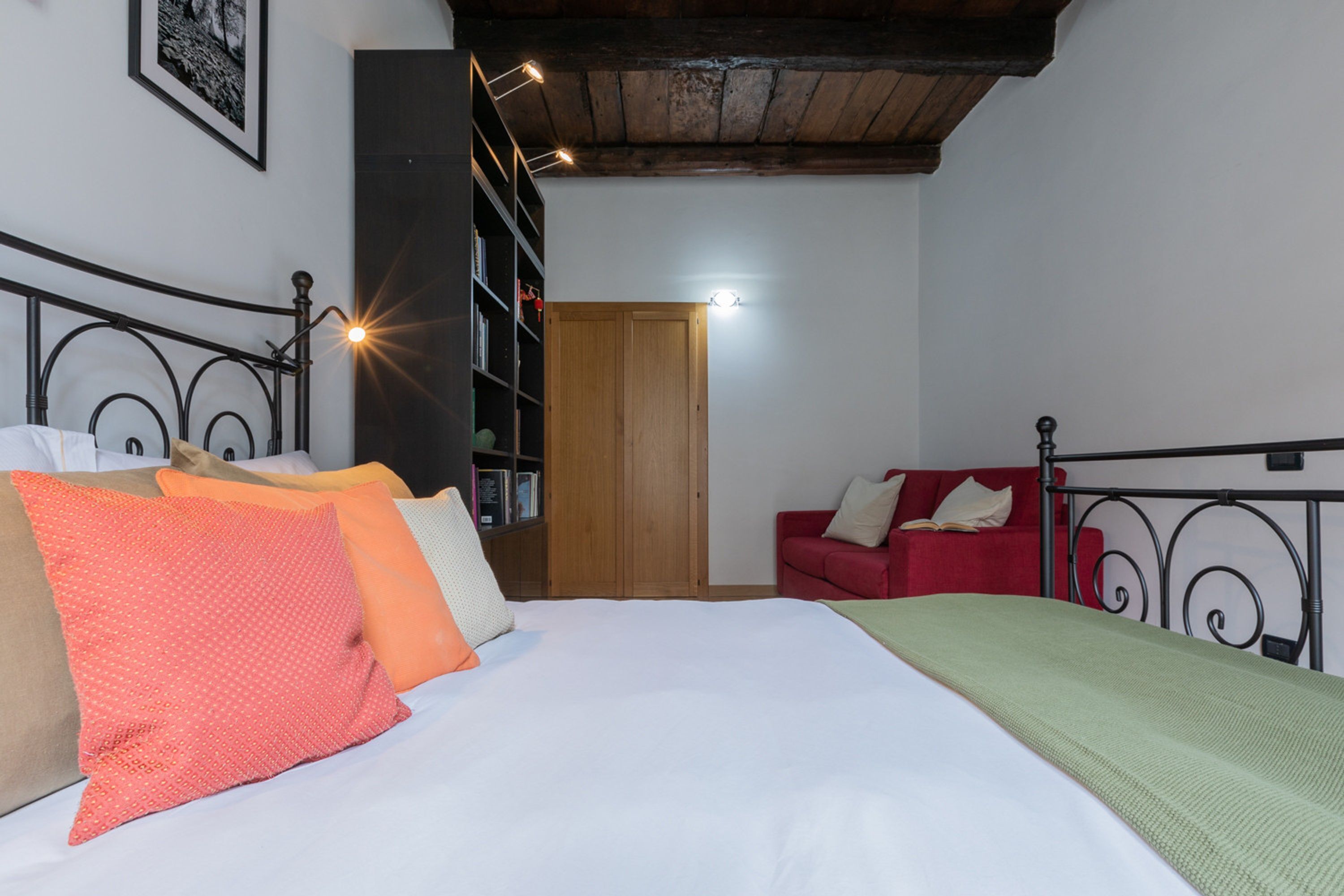 A bedroom with a bed, a red sofa, a bookshelf, and a wooden wardrobe.