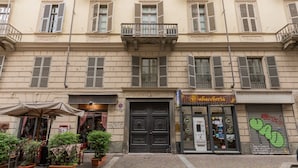 A building with a closed shop entrance, potted plants, and a cobblestone street. - La Corte by Wonderful Italy (Turin)