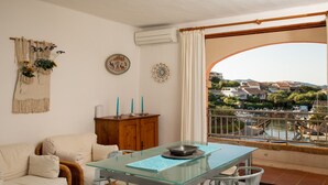 Een balkon met een glazen tafel, rieten stoelen en uitzicht op een stad en water.