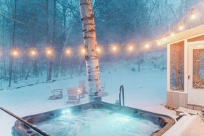 Un bain à remous dans une forêt enneigée, illuminé de guirlandes lumineuses.
