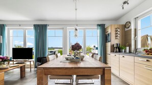 Una cocina moderna con una mesa de comedor de madera, armarios de color claro y un amplio ventanal.