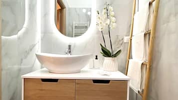 Un bagno con una parete in marmo, un lavandino bianco con un ampio specchio, cassetti in legno e una scala appoggiata al muro.