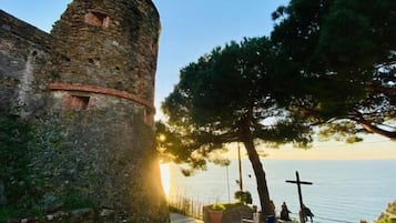 Ein Steinturm mit Kreuz, ein Pfad und ein Blick auf das Meer bei Sonnenuntergang.