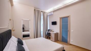 A modern hotel room with a large bed, a desk, a chair, a television, and a wardrobe.