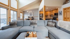 A modern living room with a sectional sofa, a wooden coffee table, and a view of the kitchen and dining area.