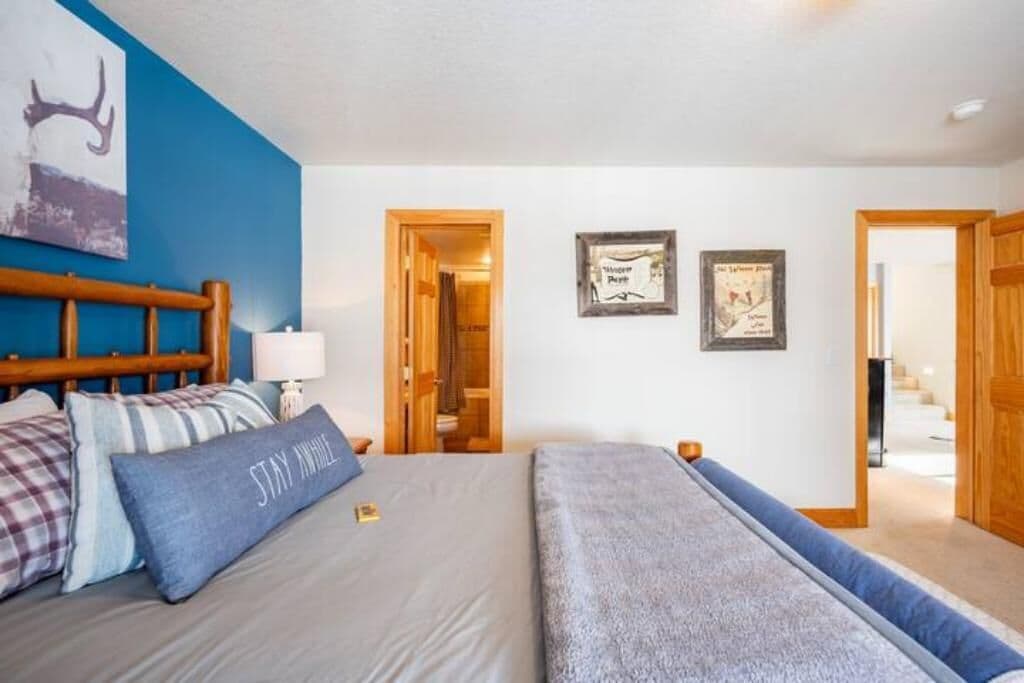 Une chambre à coucher avec un lit, des oreillers, une table de chevet, une lampe et un mur décoré de tableaux encadrés.