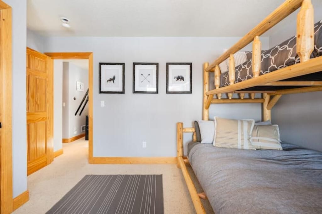 A bedroom with a bunk bed, a wooden headboard, and a gray bedspread. There are three framed pictures on the wall.