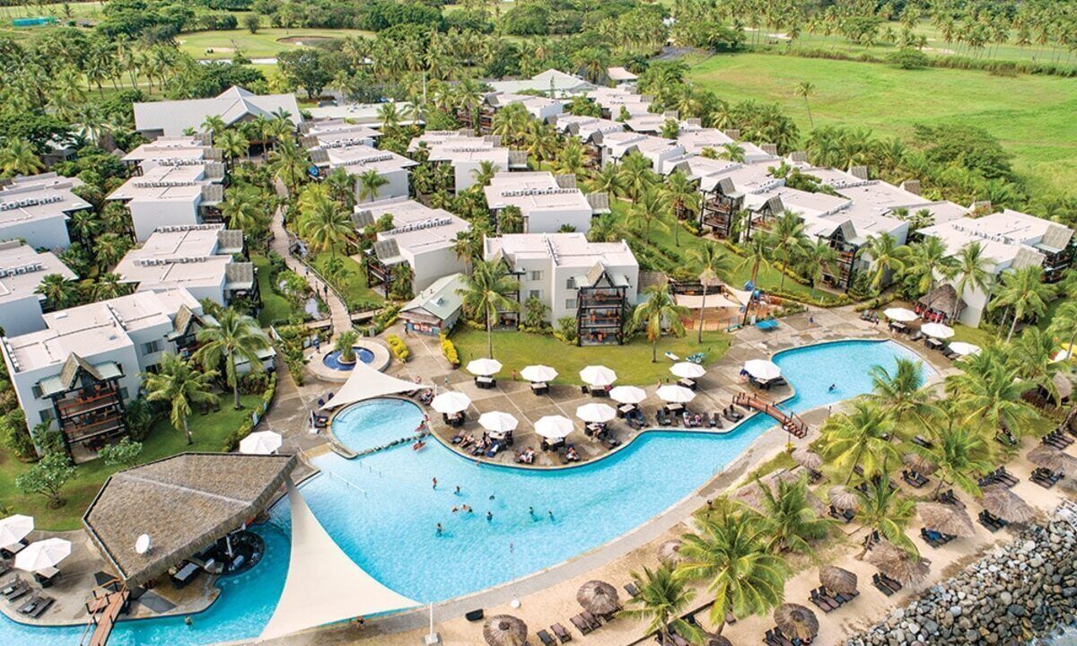 Un complexe hôtelier comprenant plusieurs bâtiments de style bungalow, une piscine centrale et de nombreux palmiers environnants.