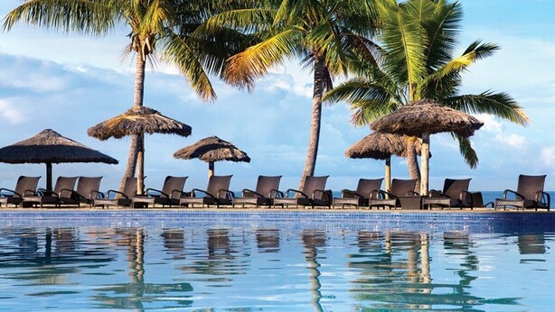 A poolside area with lounge chairs and thatched umbrellas, surrounded by palm trees. - Fiji - Whyndham -Beachfront Resort- Denarau - 2 BR (Denarau Island)