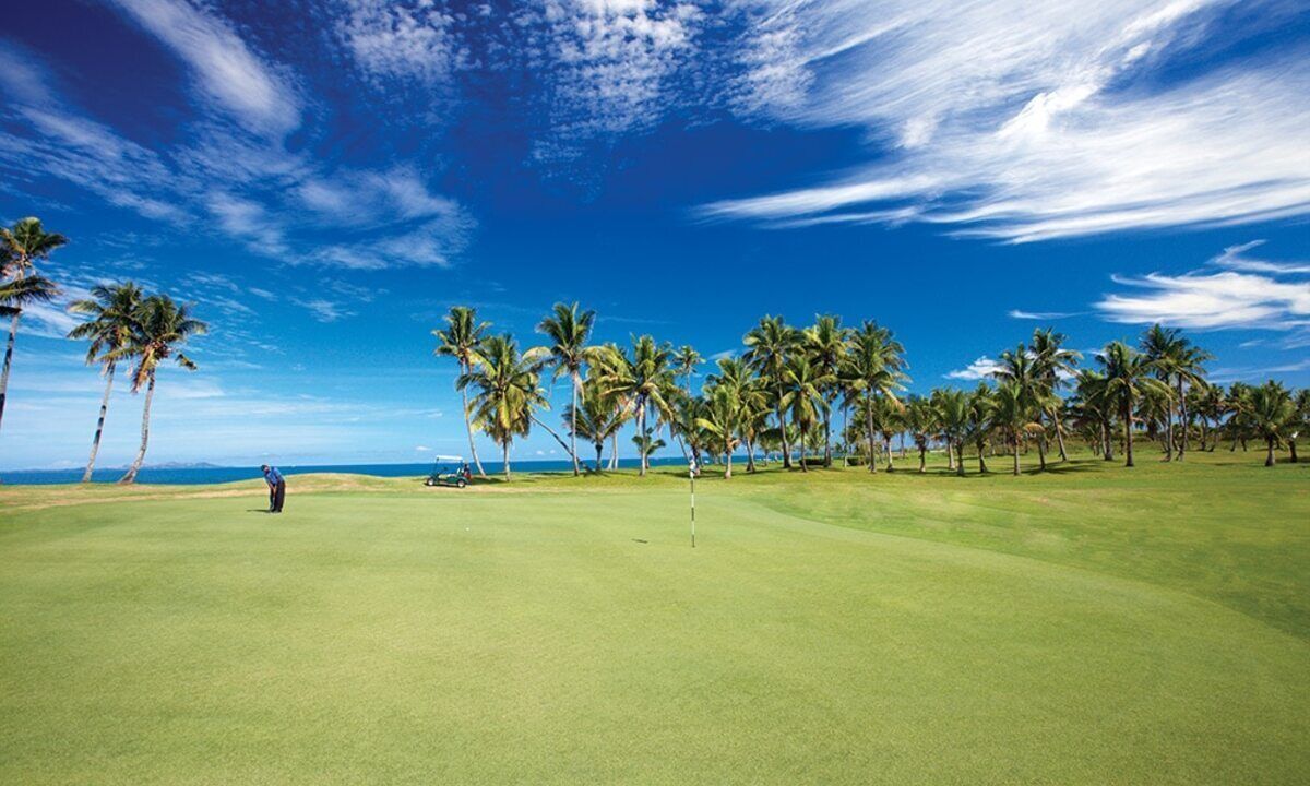 Un parcours de golf offrant une vue dégagée sur l’océan et les palmiers.