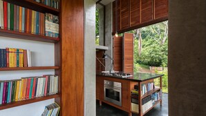 A modern kitchen with wooden cabinetry, a built-in oven, and a large window overlooking a lush garden. - Jungle Hub, private villa with pool and ocean view (Montezuma)