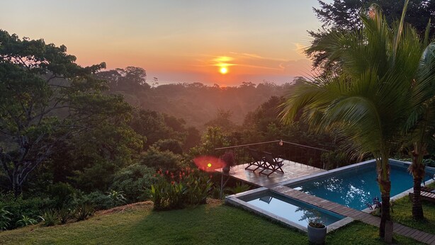 A pool area with a view of the sunset, surrounded by lush greenery and trees. - Jungle Hub, private villa with pool and ocean view (Montezuma)