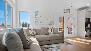 A modern living room with a beige sectional sofa, a wooden coffee table, and a large window offering a view of trees and mountains. - Moonbeam Retreat C505 |By Powder Mtn Ski Resort (Eden)
