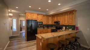 A modern kitchen with wooden cabinets, a black refrigerator, a granite countertop, and a bar area with stools. - Lakeside Funscape LS33 | Ski & Snowboard | Hot Tub (Huntsville)
