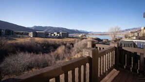 A wooden deck overlooking a mountainous landscape with a body of water and buildings in the distance. - Lakeside Funscape LS33 | Ski & Snowboard | Hot Tub (Huntsville)