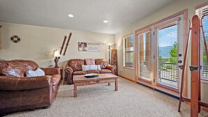 A living room with two leather sofas, a wooden coffee table, and a large sliding glass door leading to a balcony. - Eden Mtn Retreat MH207 | Near Powder Mtn | Hot Tub (Eden)