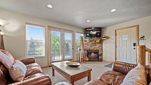 A living room with leather sofas, a stone fireplace, a flat-screen TV, and a door with a sign. - Eden Mtn Retreat MH207 | Near Powder Mtn | Hot Tub (Eden)