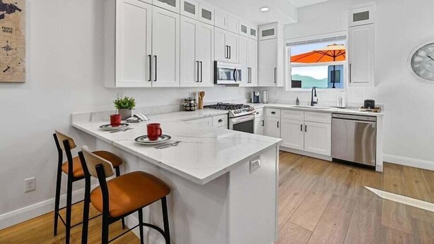Una cocina moderna con armarios blancos, una isla central con taburetes de bar, microondas, estufa y lavavajillas.