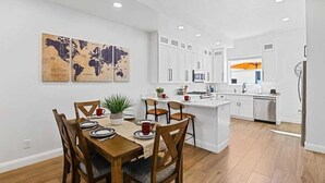 Una cocina moderna con armarios blancos, una isla central y un comedor con sillas y mesa de madera.