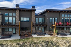 A modern multi-story building with stone and wood accents, large windows, and outdoor seating areas. - Moose Ridge Hideaway Ri903 | Ski Retreat | Hot Tub (Eden)