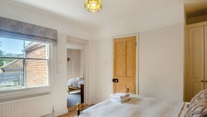A bedroom with a large bed, a wooden door, and a window overlooking a brick wall. - 3 bedroom accommodation in Overstrand, near Cromer (Overstrand, near Cromer)