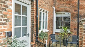 A brick house with two windows and a door, a small garden area with two wicker chairs and potted plants. - 3 bedroom accommodation in Overstrand, near Cromer (Overstrand, near Cromer)