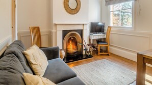 A living room with a fireplace, a sofa, a desk with a computer, and a window with a view of the outside. - 3 bedroom accommodation in Overstrand, near Cromer (Overstrand, near Cromer)