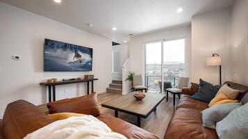 A modern living room with a large window, a sofa, a coffee table, and a painting on the wall.