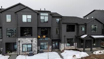 A modern multi-story building with a grey exterior, a stone fireplace, and a covered outdoor seating area.