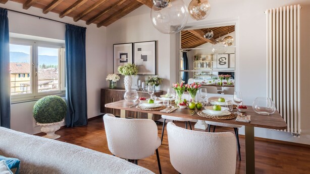 A dining area with a wooden table set for four, a potted plant, and a view of the city through a window.