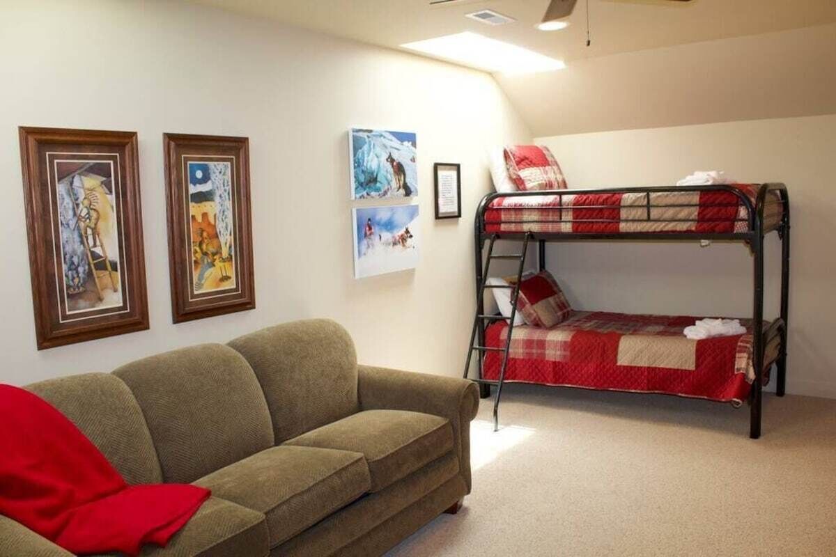 Una habitación con una cama individual superpuesta, un sofá y cuadros en la pared.