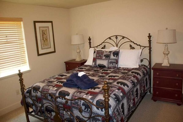 A bedroom with a bed, two nightstands, a dresser, a window with blinds, and a framed picture on the wall.
