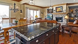 A spacious kitchen with a large island, wooden cabinetry, and a stone fireplace. - Powder Mtn Wolf Den TR11|Mtn Biking |Dog Friendly (Eden)