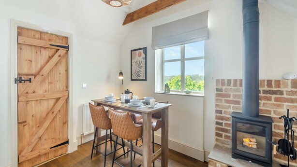 A dining area with a wooden table, leather chairs, a hanging light fixture, a window with a view, and a wood-burning stove. - We love the views from the garden across open countryside. (Seaton, near Hornsea)