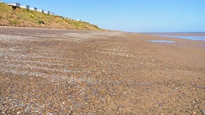 A pebbled beach with houses on a grassy hill in the background. - We love the views from the garden across open countryside. (Seaton, near Hornsea)