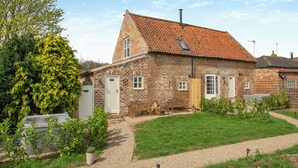 A brick house with a sloped roof, a front door, and a small garden area with a pathway. - We love the views from the garden across open countryside. (Seaton, near Hornsea)