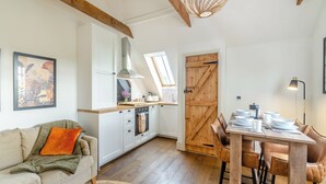A cozy kitchen with wooden beams, a dining area with a table and chairs, and a large window. - We love the views from the garden across open countryside. (Seaton, near Hornsea)