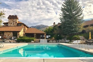 A swimming pool with a stone building and mountains in the background.
