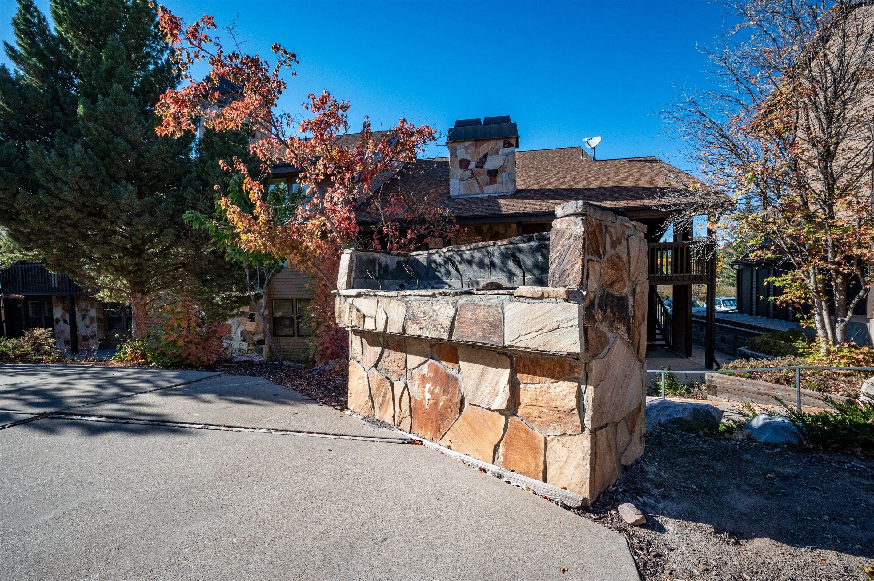 A stone wall with a fireplace, surrounded by trees and a clear blue sky.