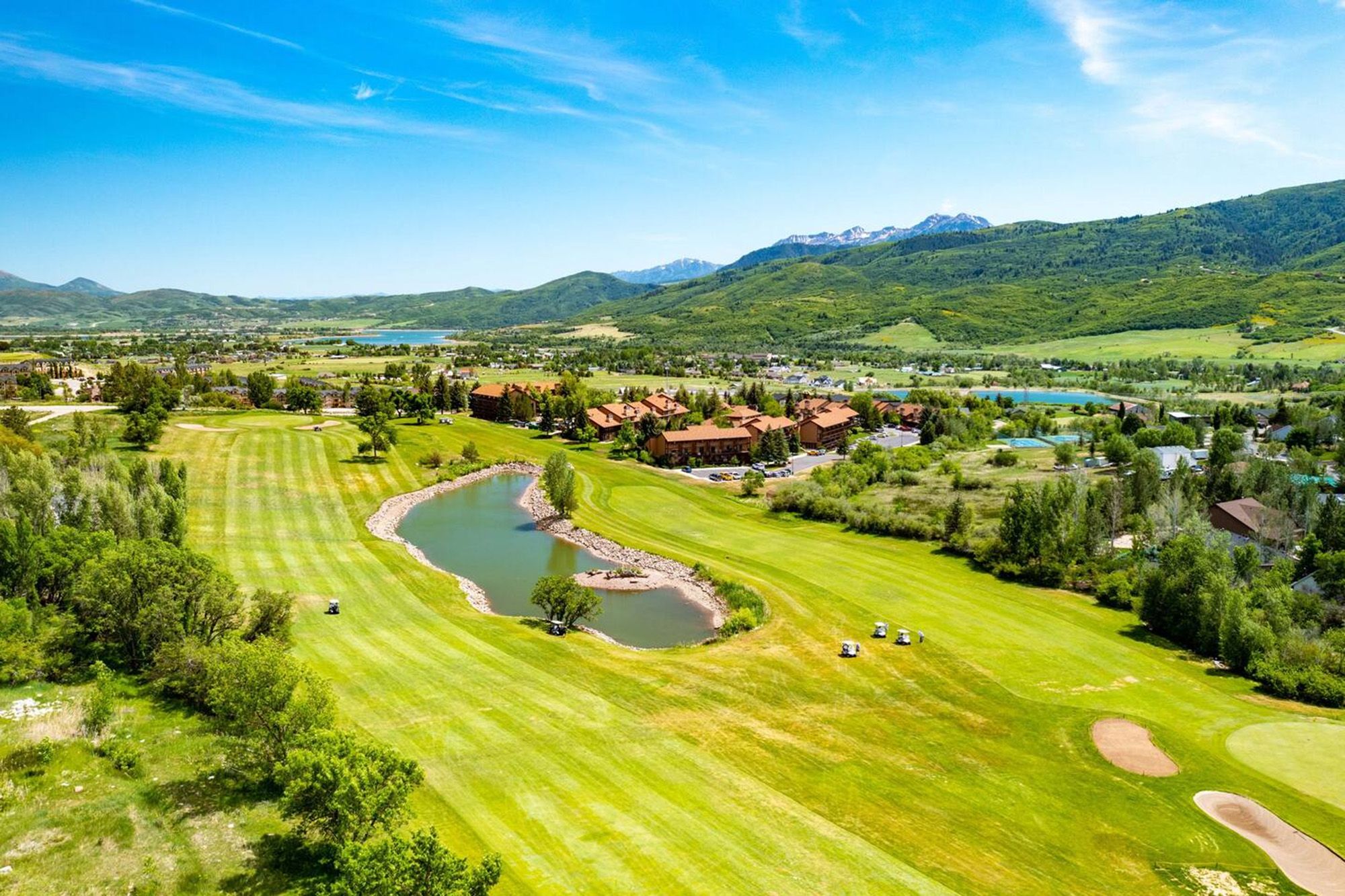 A golf course with a lake, surrounded by residential buildings and mountains.