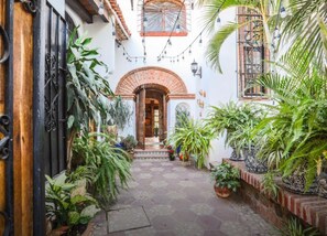 A narrow courtyard with a tiled floor, surrounded by potted plants and a wooden door. - Beautiful home in Zona Dorado Bucerias, 2 blocks from beach with ocean views (Bucerias)