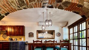 Cuina àmplia amb arc de pedra, armaris de fusta, terra de rajola i zona de menjador amb cadirees i taula.