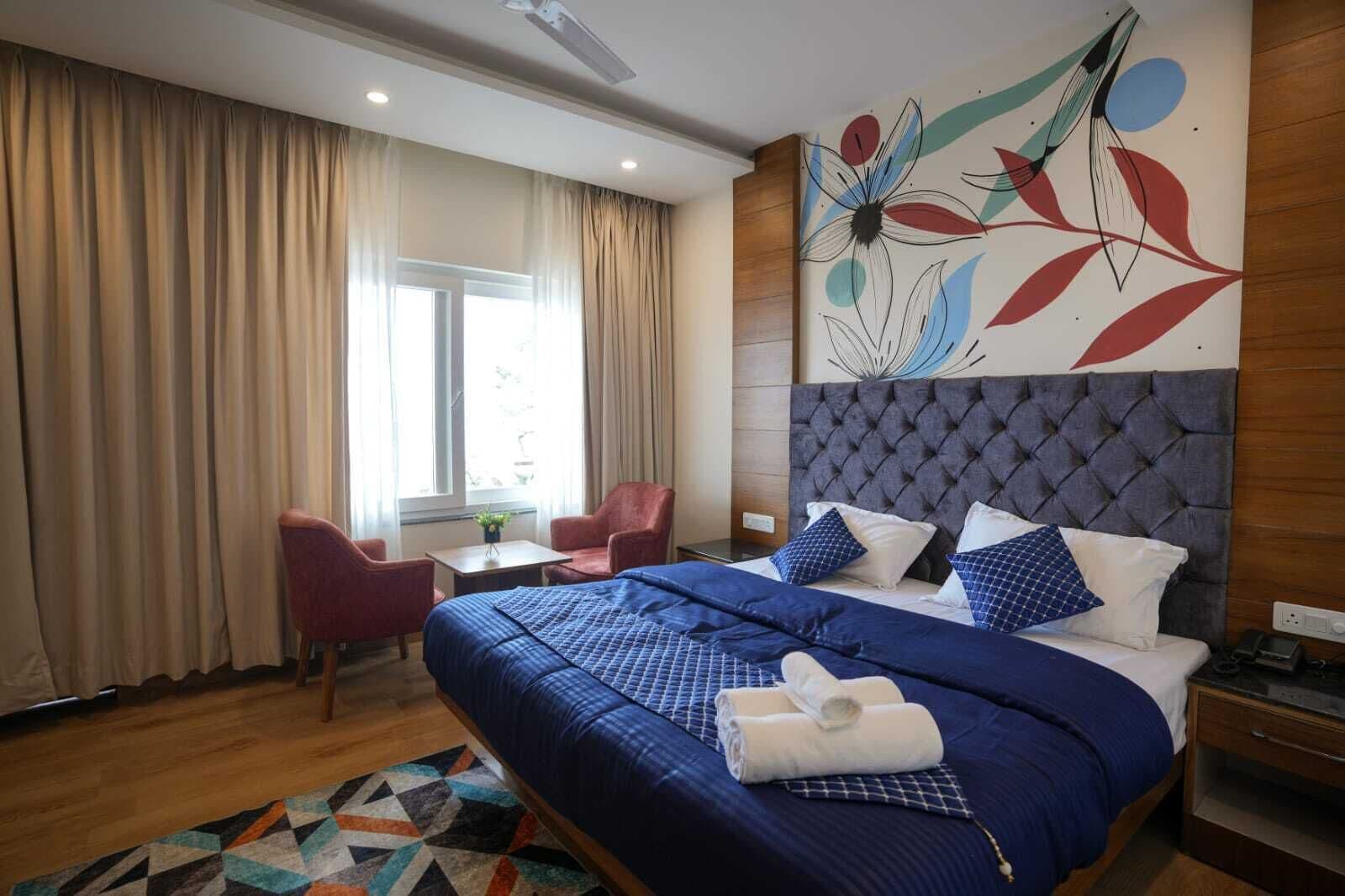 A hotel room with a large bed, a headboard, a desk, a chair, and a window with curtains.