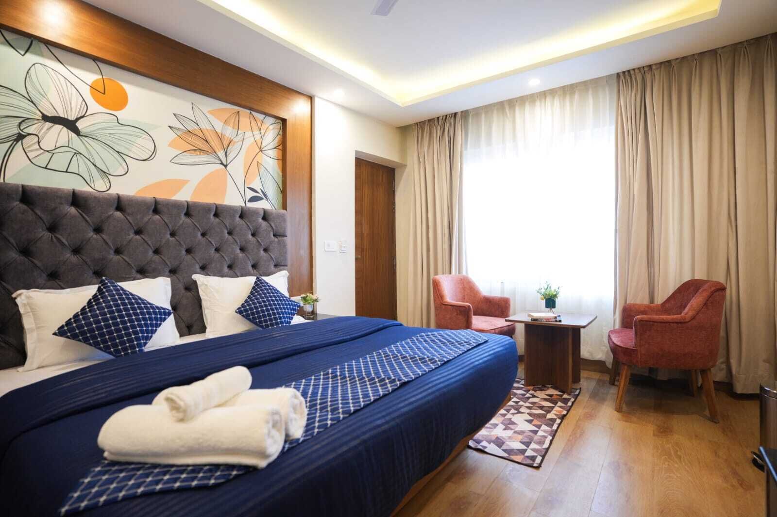 Une chambre d’hôtel avec un grand lit, deux fauteuils, une petite table et un tableau au mur.