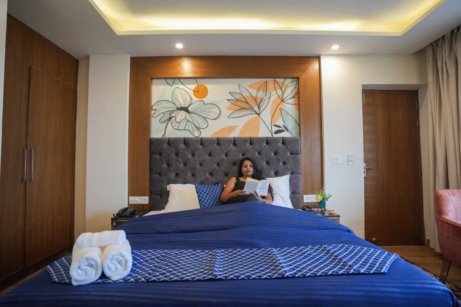 A hotel room with a large bed, a tufted headboard, a decorative wall art, and wooden wardrobes.