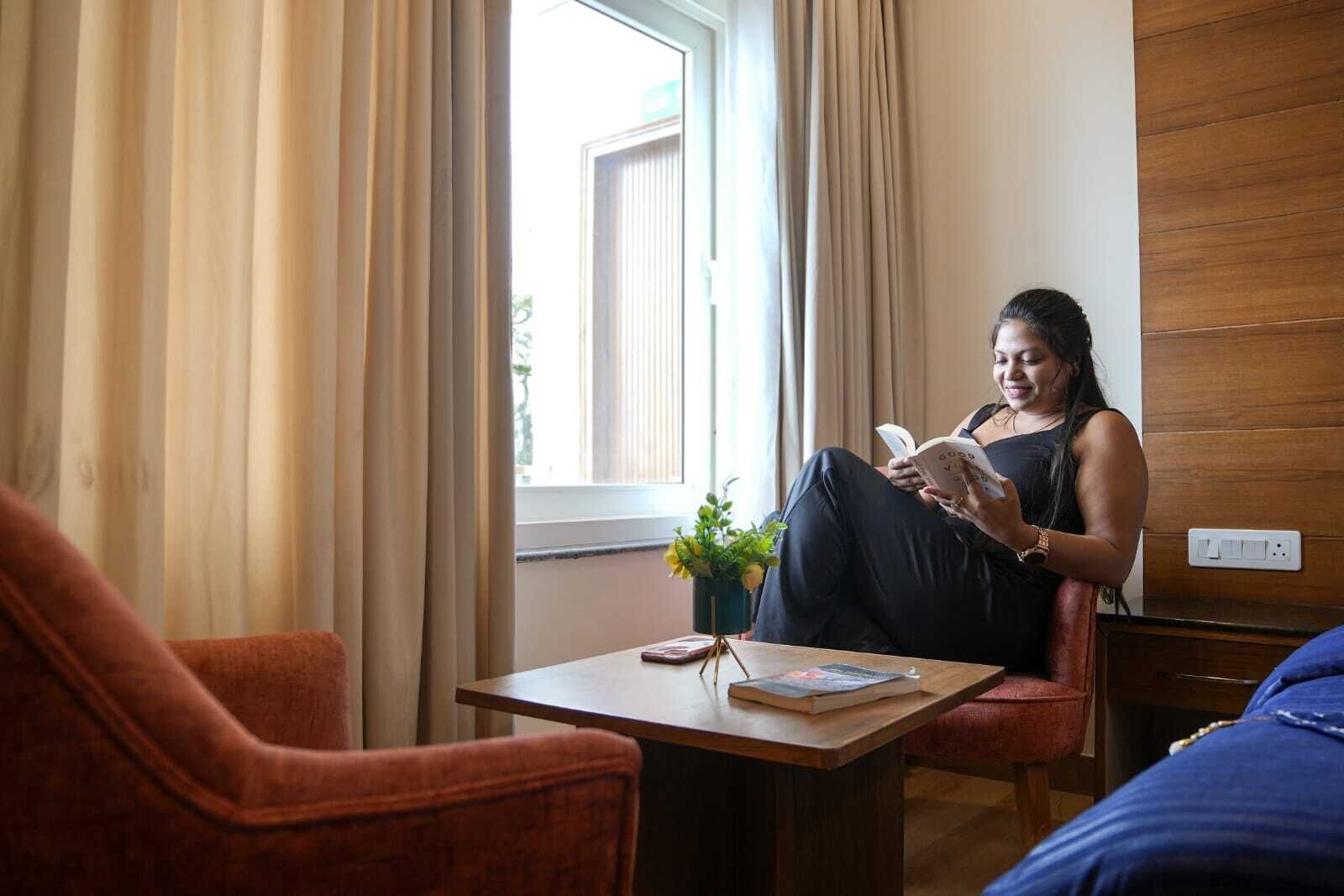 A room with a bed, a chair, a small table, and a window with curtains.