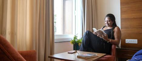 A room with a bed, a chair, a small table, and a window with curtains.